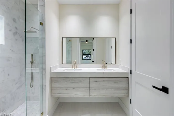 This master bath features a spacious shower, dual sinks, and stunning marble tiles throughout. The modern LED mirror adds a stylish touch, enhancing both the design and functionality of the space.
