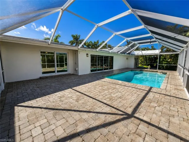 Screened pool enclosure featuring a swimming pool, extensive paver patio, and multiple sliding glass doors