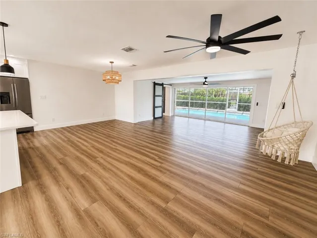 Open-concept living space featuring wood-finish flooring, a contemporary ceiling fan, and sliding glass doors revealing a screened pool area