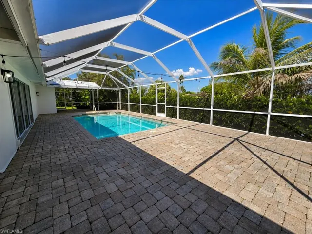 Screened lanai featuring a swimming pool, expansive paver patio, and mature tropical landscaping
