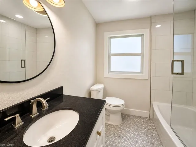 Black countertop vanity with an undermount sink, round mirror, and a walk-in shower with a glass enclosure
