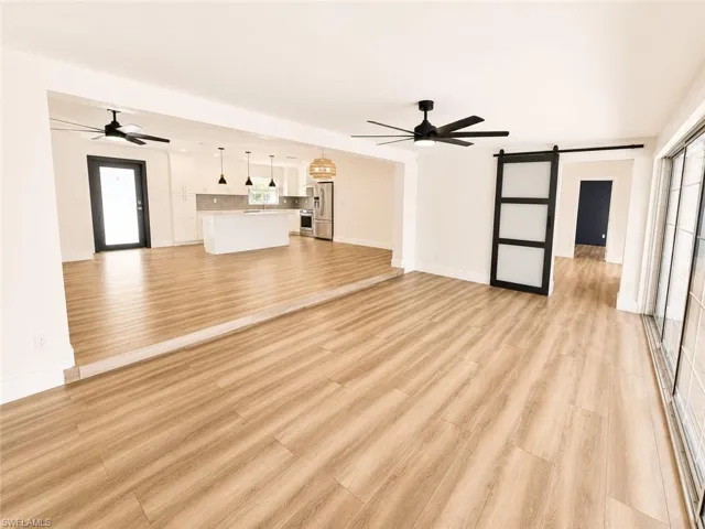 Wood-finish flooring throughout, modern kitchen with white cabinetry and stainless steel appliances, contemporary ceiling fans, sliding barn door, and large sliding glass doors