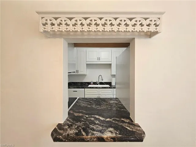 Kitchen featuring white cabinetry, stainless steel refrigerator, white dishwasher, and dark stone counters