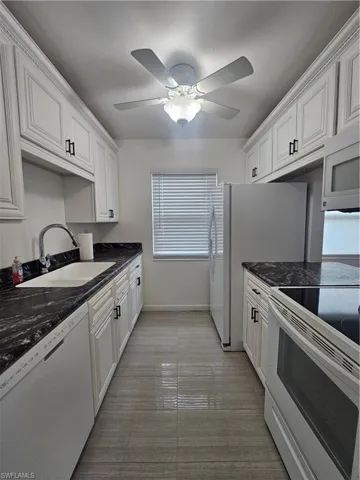 Kitchen with stainless steel stove, dishwasher, dark stone countertops, and white cabinetry
