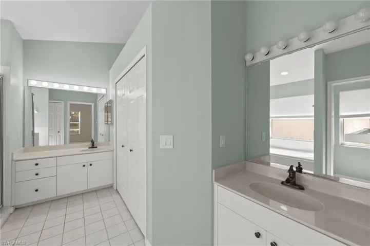 Full bathroom featuring two vanities, light tile patterned floors, and a closet