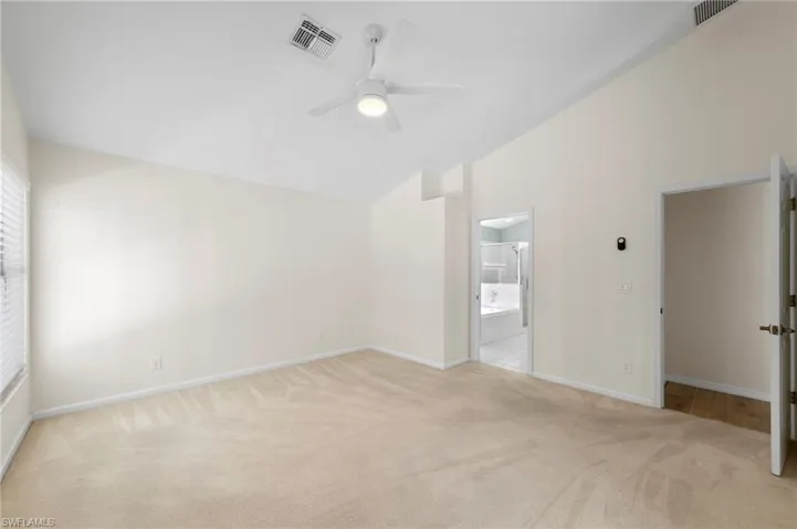 Unfurnished bedroom featuring light colored carpet, a ceiling fan, ensuite bathroom, and high vaulted ceiling