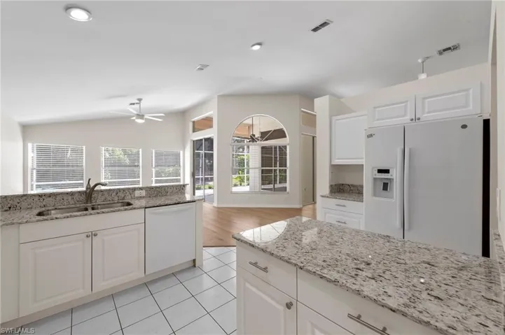 Kitchen with light stone countertops, white appliances, white cabinetry, lofted ceiling, and light tile patterned flooring