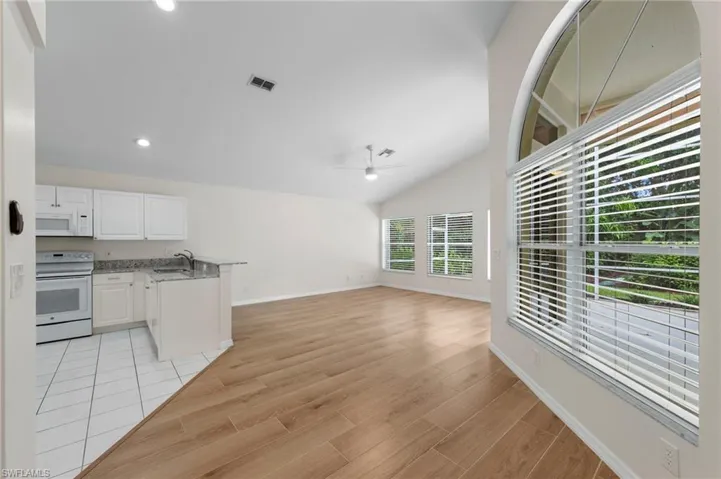 Kitchen featuring a peninsula, white appliances, white cabinets, lofted ceiling, and light wood-style flooring