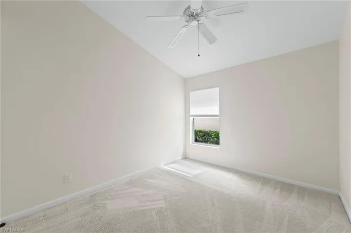 Carpeted empty room with lofted ceiling and a ceiling fan