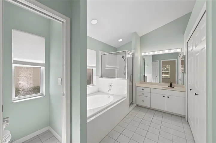 Full bath with vanity, a stall shower, a bath, light tile patterned floors, and vaulted ceiling