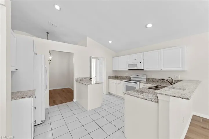 Kitchen featuring a peninsula, white cabinets, light stone counters, vaulted ceiling, and recessed lighting