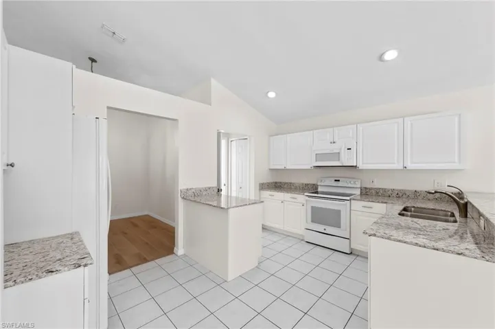Kitchen with light stone countertops, white appliances, a peninsula, vaulted ceiling, and recessed lighting