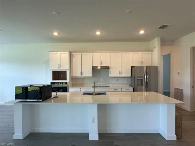 Kitchen featuring a kitchen island with sink, white cabinets, and stainless steel appliances