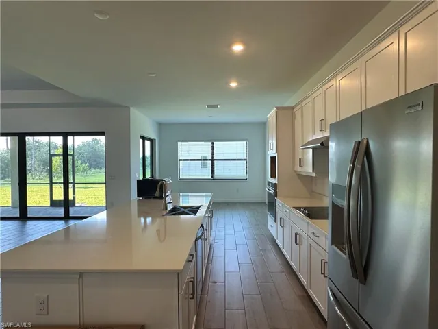 Kitchen with stainless steel refrigerator with ice dispenser, dark hardwood / wood-style floors, black electric stovetop, a center island with sink, and sink