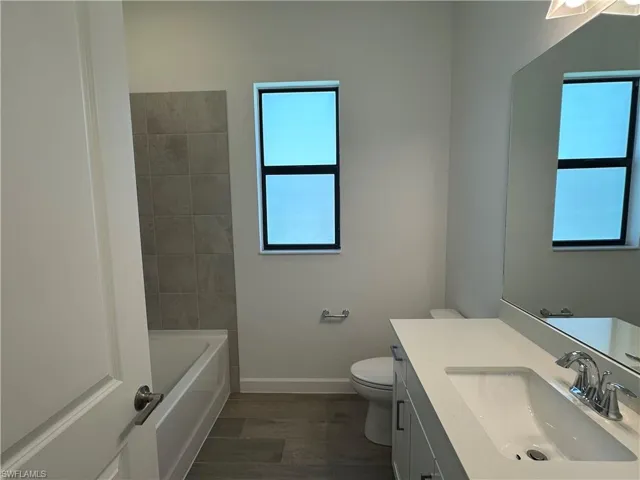 Full bathroom featuring vanity, toilet, tiled shower / bath combo, and hardwood / wood-style flooring
