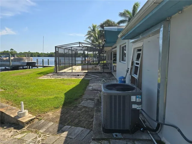 View of grassy yard with a water view, a patio, glass enclosure, and a boat dock