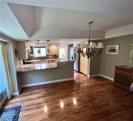 Kitchen featuring light stone countertops, kitchen peninsula, hardwood / wood-style floors, decorative light fixtures, and an inviting chandelier