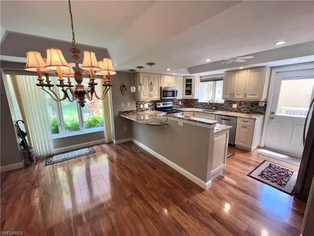 Kitchen with appliances with stainless steel finishes, decorative light fixtures, backsplash, and wood-type flooring