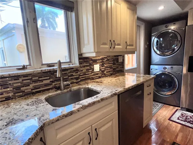 Kitchen featuring light hardwood / wood-style flooring, stacked washer and clothes dryer, light stone counters, dishwashing machine, and tasteful backsplash