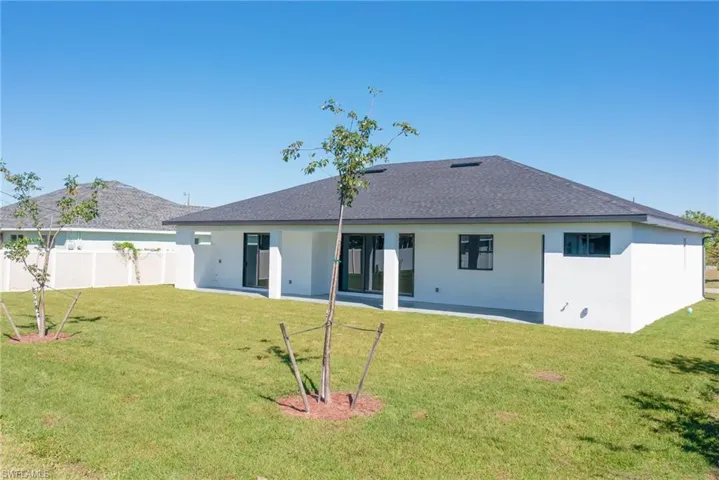 Rear view of property with a shingled roof, a yard, fence, and stucco siding