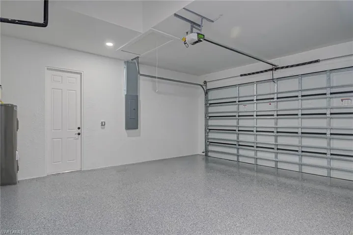 Garage with recessed lighting, electric panel, a garage door opener, and water heater