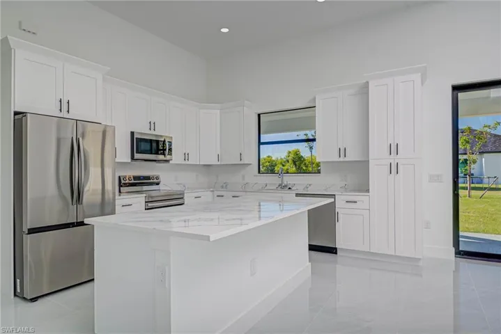Kitchen with light stone counters, a sink, a center island, appliances with stainless steel finishes, and white cabinets