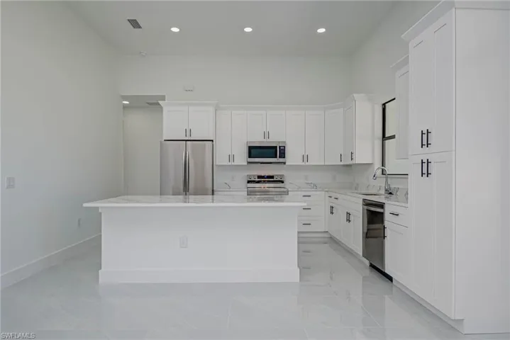 Kitchen featuring a sink, stainless steel appliances, white cabinetry, marble finish floor, and a center island