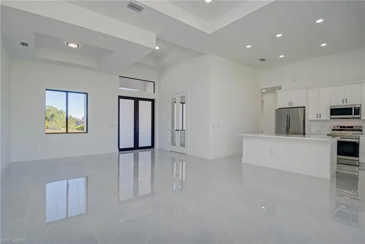 Kitchen featuring open floor plan, a towering ceiling, white cabinets, stainless steel appliances, and a raised ceiling