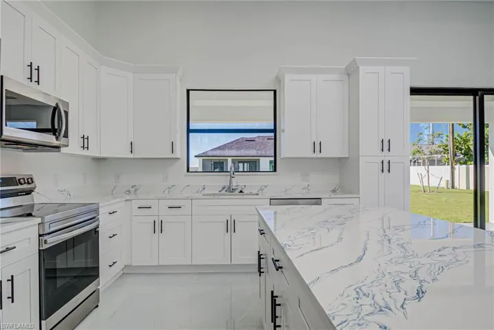 Kitchen featuring white cabinets, appliances with stainless steel finishes, light stone countertops, and a sink