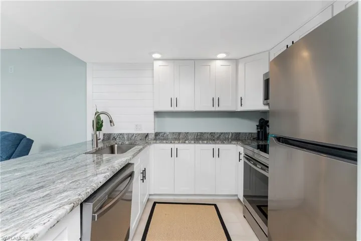 Kitchen featuring stainless steel appliances, light stone countertops, white cabinetry, recessed lighting, and a peninsula