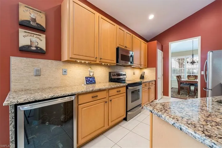 Kitchen with wine cooler, stainless steel appliances, lofted ceiling, backsplash, and light tile floors