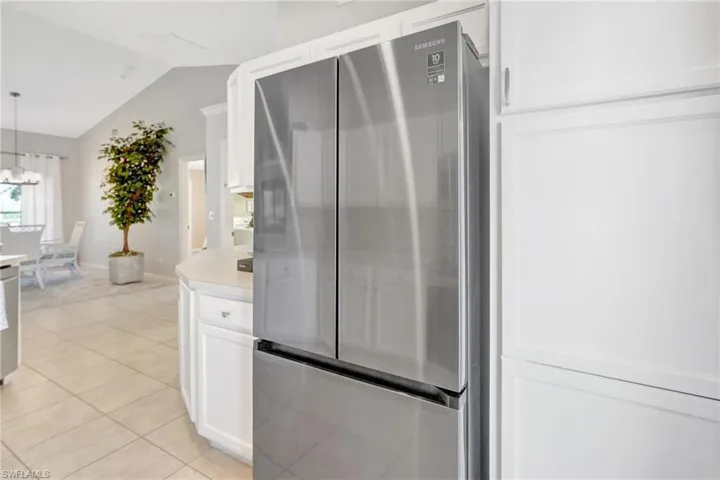 Kitchen featuring a notable chandelier, vaulted ceiling, light tile patterned floors, white cabinetry, and freestanding refrigerator