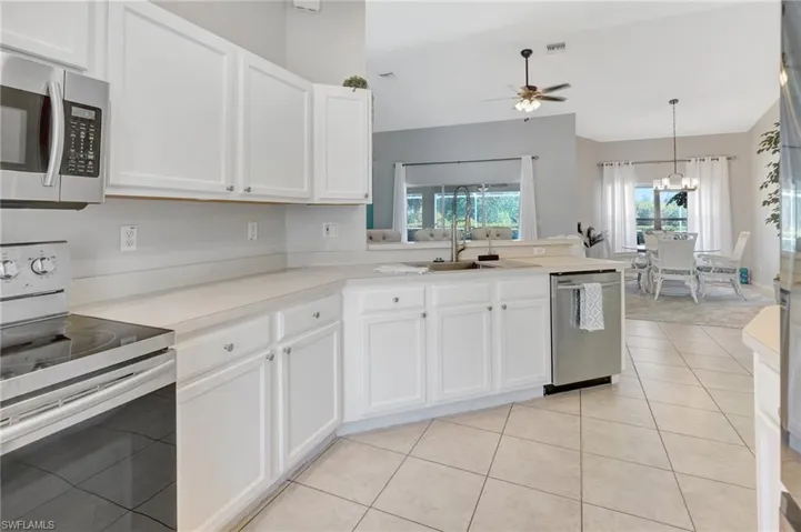 Kitchen with a ceiling fan, light tile patterned flooring, white cabinets, appliances with stainless steel finishes, and a sink