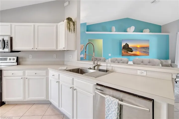 Kitchen featuring light tile patterned floors, a sink, appliances with stainless steel finishes, white cabinetry, and lofted ceiling