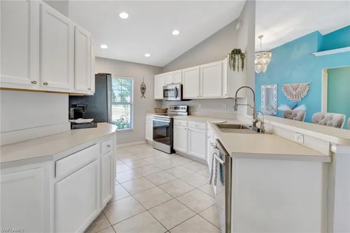 Kitchen with light tile patterned floors, appliances with stainless steel finishes, light countertops, a sink, and lofted ceiling