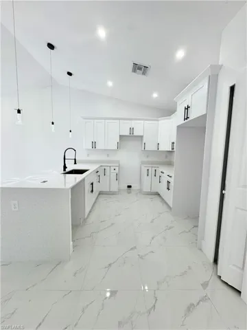 Kitchen featuring white cabinetry, lofted ceiling, light stone counters, hanging light fixtures, and a peninsula