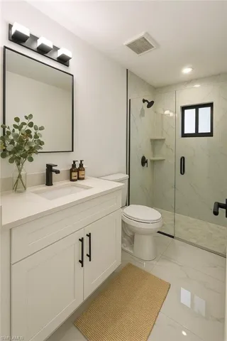 Bathroom featuring a marble finish shower, vanity, light marble finish floors, and recessed lighting