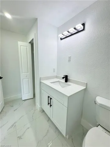 Half bath with vanity, light marble finish floors, and a textured wall