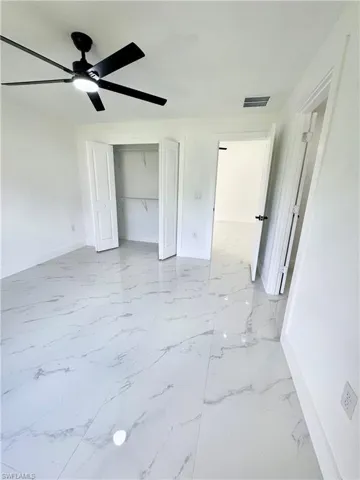 Unfurnished bedroom featuring light marble finish flooring, a ceiling fan, and a closet
