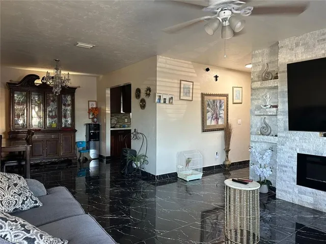 Living room featuring ceiling fan with notable chandelier, a textured ceiling, and a fireplace