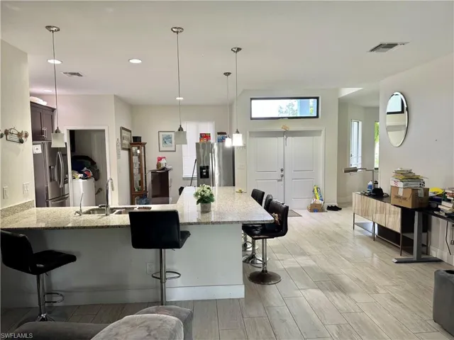 Kitchen with a kitchen bar, a peninsula, light stone counters, stainless steel refrigerator with ice dispenser, and recessed lighting