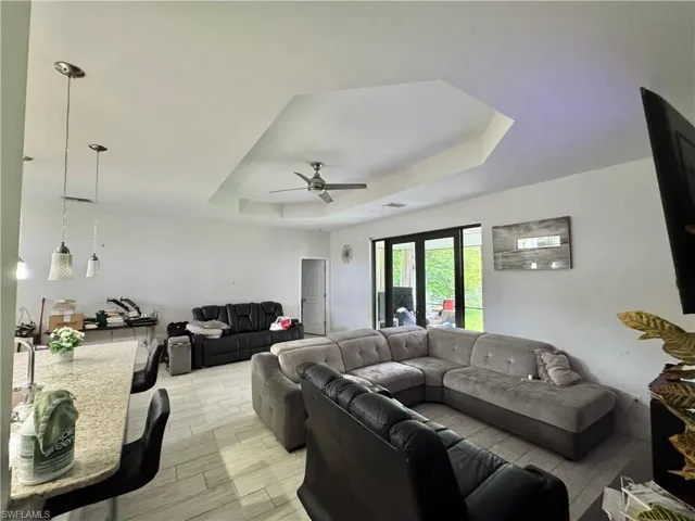 Living room featuring a tray ceiling, light wood-style flooring, and a ceiling fan