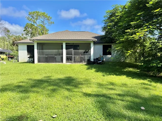Rear view of house with a shingled roof, a yard, stucco siding, and a sunroom
