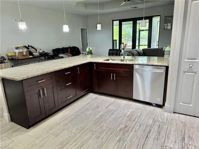 Kitchen featuring open floor plan, light stone countertops, dishwasher, and pendant lighting