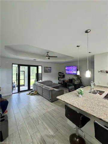 Living area with a raised ceiling, a ceiling fan, and wood finish floors