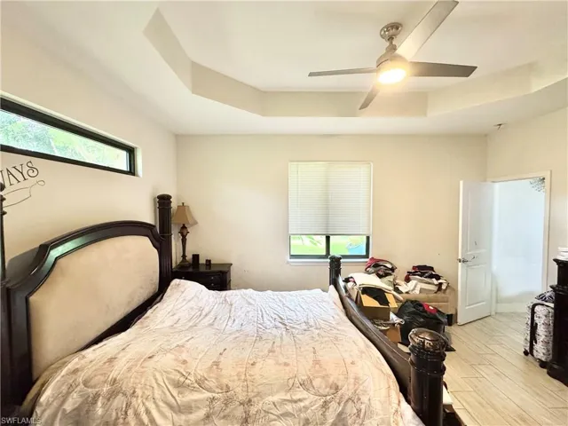 Bedroom featuring a raised ceiling, ceiling fan, and light wood finished floors
