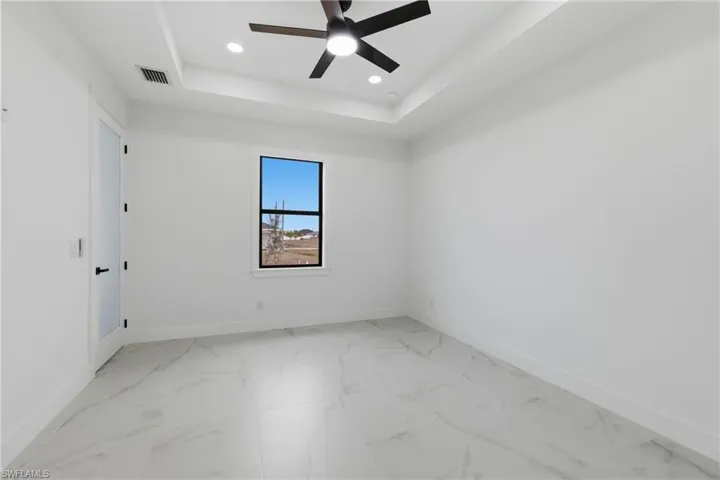 Spare room with a tray ceiling, recessed lighting, light marble finish flooring, and a ceiling fan