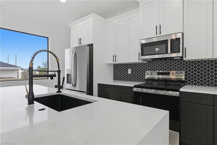 Kitchen with white cabinetry, appliances with stainless steel finishes, light stone countertops, backsplash, and recessed lighting