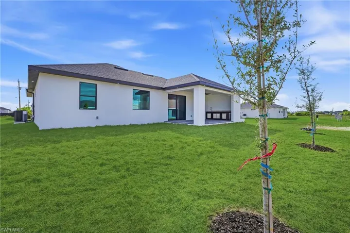 Back of house with stucco siding, a patio area, a yard, and a shingled roof