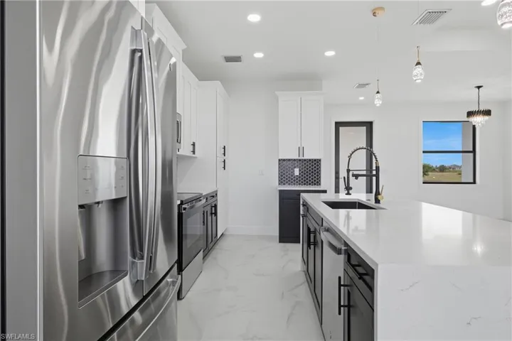 Kitchen with stainless steel appliances, white cabinetry, decorative light fixtures, recessed lighting, and light stone countertops
